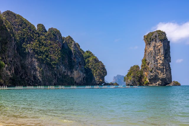 Vue depuis la plage d'Ao Nang à Krabi, montrant un ponton flottant et les célèbres falaises karstiques de la mer d'Andaman en arrière-plan.