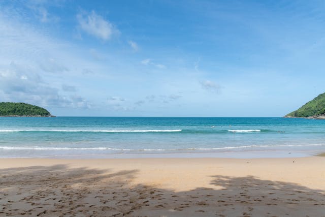 Vaste étendue de sable fin sur la plage de Nai Harn à Phuket, avec une mer calme sous un ciel bleu, reflétant l'atmosphère relaxante de la baie.