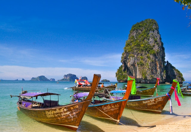 Bateaux long-tail traditionnels amarrés sur le sable blanc de la plage de Phra Nang, avec une falaise karstique en arrière-plan à Krabi, Thaïlande.