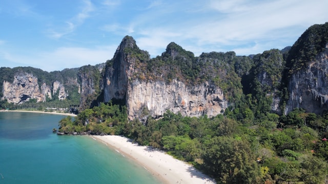 Vue aérienne de la plage de sable blanc de Railay à Krabi, entourée de falaises karstiques et d'une eau turquoise, sous un ciel bleu.