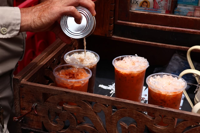 Un vendeur prépare un Cha Yen (thé glacé thaïlandais) en versant du lait concentré dans un gobelet rempli de glace.