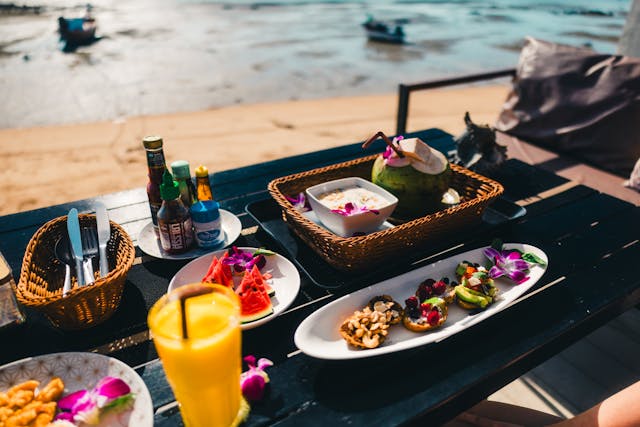 Table dressée pour un repas avec une noix de coco, des fruits et des plats thaïlandais, en bord de mer sur une plage de Thaïlande.