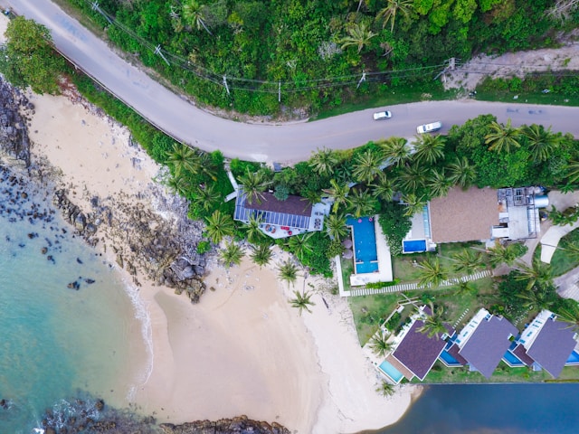 Vue de drone de la route côtière de Koh Lanta, serpentant entre la jungle et les hôtels en bord de mer avec leurs piscines.