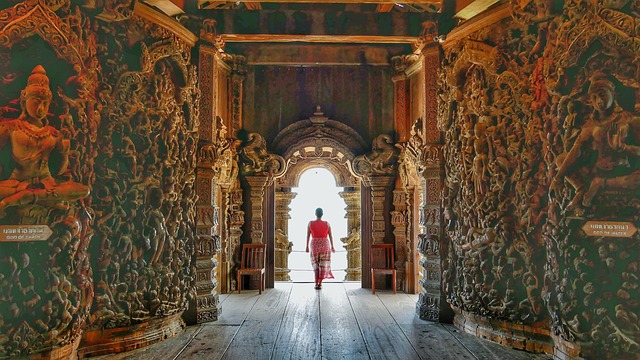 Femme en tenue respectueuse marchant dans le couloir en bois richement sculpté du Sanctuaire de la Vérité à Pattaya, illustrant le savoir-vivre en Thaïlande.