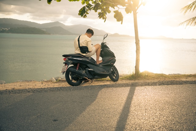 Voyageur faisant une pause sur un scooter devant un lac et des montagnes sur la route de Pai, au nord de la Thaïlande.