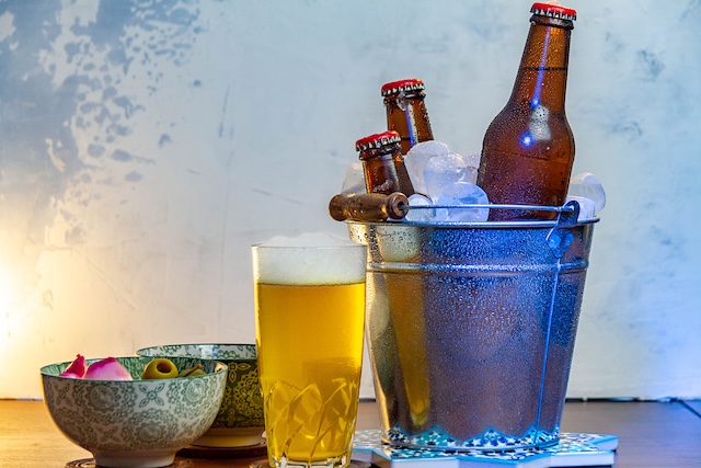 Un seau en métal rempli de glace et de bouteilles de bière, à côté d'un verre de bière blonde servi.