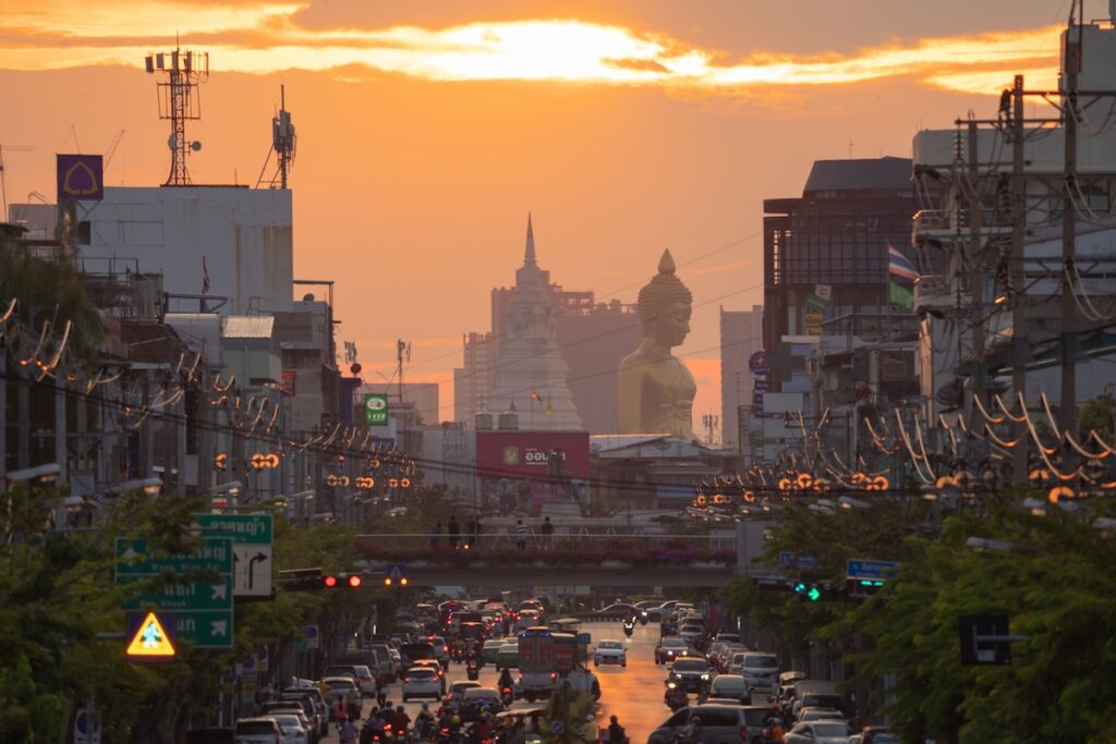 Vue du trafic dense de Bangkok au coucher du soleil avec la grande statue du Bouddha du Wat Paknam, illustrant les contrastes de la sécurité en Thaïlande.