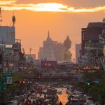 Vue du trafic dense de Bangkok au coucher du soleil avec la grande statue du Bouddha du Wat Paknam, illustrant les contrastes de la sécurité en Thaïlande.