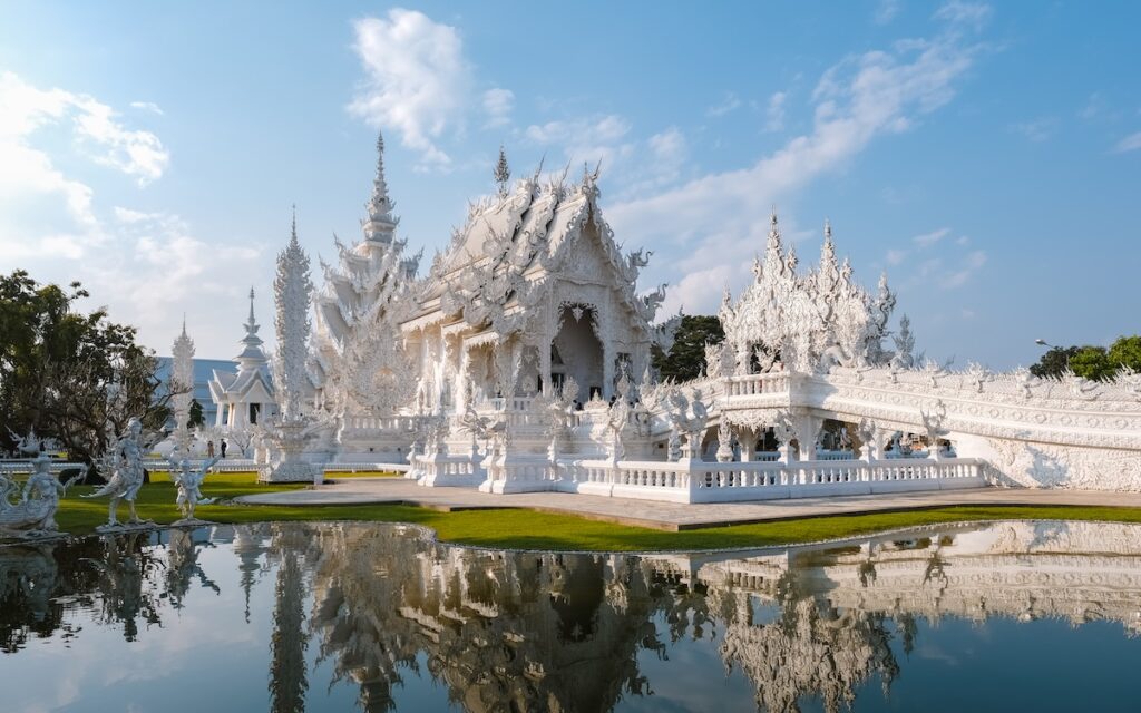 Vue du Temple Blanc de Chiang Rai (Wat Rong Khun) et son pont, se reflétant dans l'eau par une journée ensoleillée.
