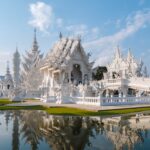 Vue du Temple Blanc de Chiang Rai (Wat Rong Khun) et son pont, se reflétant dans l'eau par une journée ensoleillée.