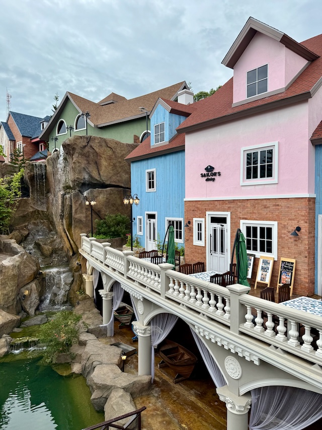 Terrasse du restaurant Sailor's Dining au Fisherman Village Pattaya, avec des bâtiments colorés et une cascade artificielle en arrière-plan.