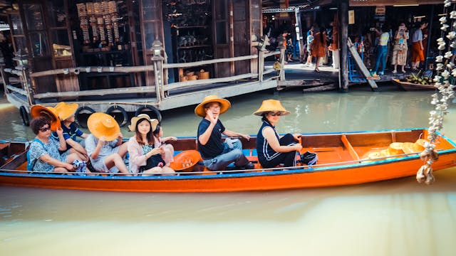 Un groupe de touristes souriants sur un bateau long-tail naviguant dans un marché flottant animé en Thaïlande, illustrant une interaction amicale.