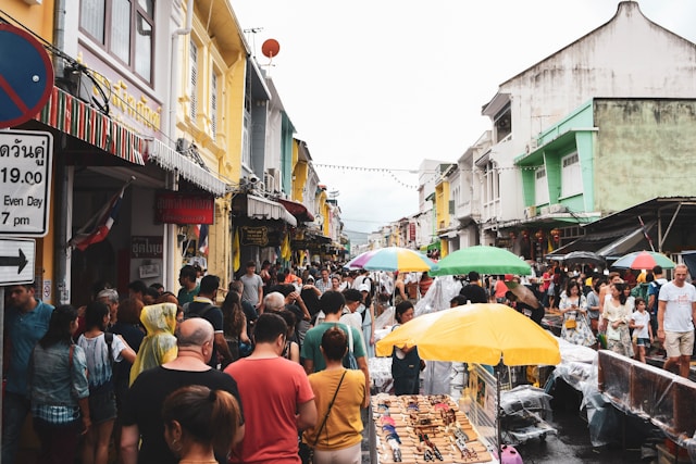 Foule de touristes et de locaux dans une rue animée de la vieille ville de Phuket, bordée de bâtiments colorés et de stands de marché.
