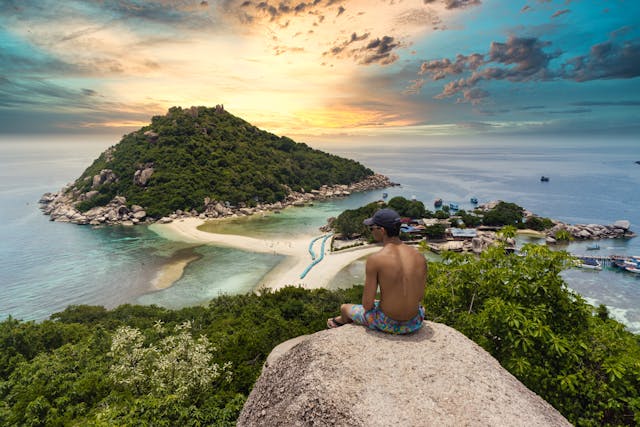 Voyageur assis sur un rocher contemplant la vue panoramique sur l'île de Koh Nang Yuan en Thaïlande au coucher du soleil.