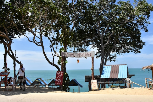 Un restaurant local et rustique en bord de route à Koh Lanta, avec une enseigne en bois "Richard Restaurant" et une vue sur la mer turquoise.
