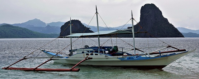 Bateau traditionnel philippin (bangka) amarré dans une baie aux eaux calmes, avec en arrière-plan les célèbres falaises de calcaire de l'archipel des Philippines.