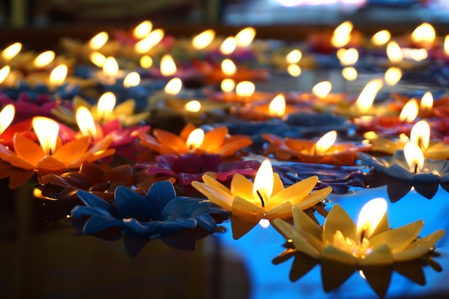 Gros plan sur de nombreuses bougies colorées en forme de fleurs de lotus, flottant et illuminant l'eau pendant le festival de Loi Krathong.
