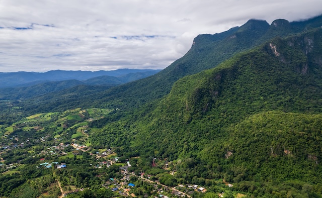 Vue aérienne du village de Chiang Dao niché dans une vallée verdoyante au pied de l'imposant massif montagneux de Doi Luang Chiang Dao sous un ciel nuageux.
