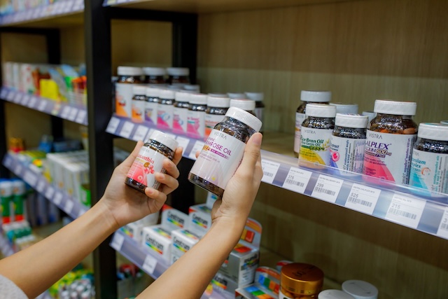 Une personne tenant et comparant deux flacons de médicaments dans les rayons d'une pharmacie bien achalandée en Thaïlande.