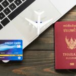 Passeport thaïlandais, carte bancaire et un avion miniature posés sur un ordinateur portable, symbolisant la préparation de l'assurance voyage pour la Thaïlande.
