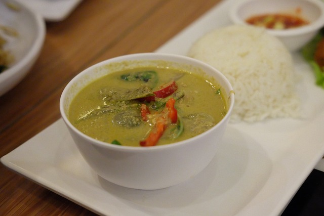 Un bol de curry vert thaïlandais, plat emblématique de la gastronomie thaïe, garni de piments rouges et servi avec du riz blanc.