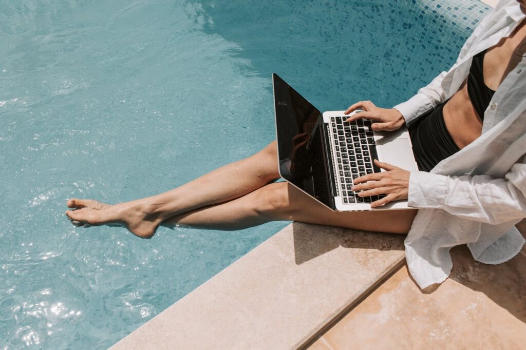 Une femme, digital nomad en Thaïlande, travaillant sur son ordinateur portable les pieds dans l'eau d'une piscine.