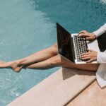 Une femme, digital nomad en Thaïlande, travaillant sur son ordinateur portable les pieds dans l'eau d'une piscine.