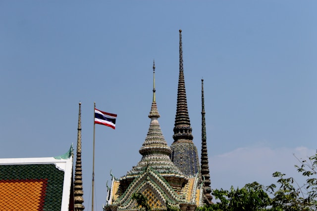Le drapeau thaïlandais flottant à côté des chedis décorés d'un temple bouddhiste à Bangkok sous un ciel bleu.