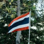 Le drapeau national de la Thaïlande, le Thong Trairong, flottant dans un jardin avec des arbres en arrière-plan.