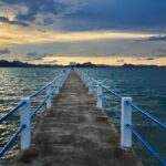 Un long embarcadère en béton s'avançant dans la mer en Thaïlande, invitant à découvrir des îles hors des sentiers battus au coucher du soleil.