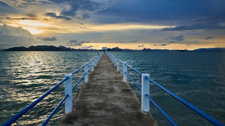 Un long embarcadère en béton s'avançant dans la mer en Thaïlande, invitant à découvrir des îles hors des sentiers battus au coucher du soleil.
