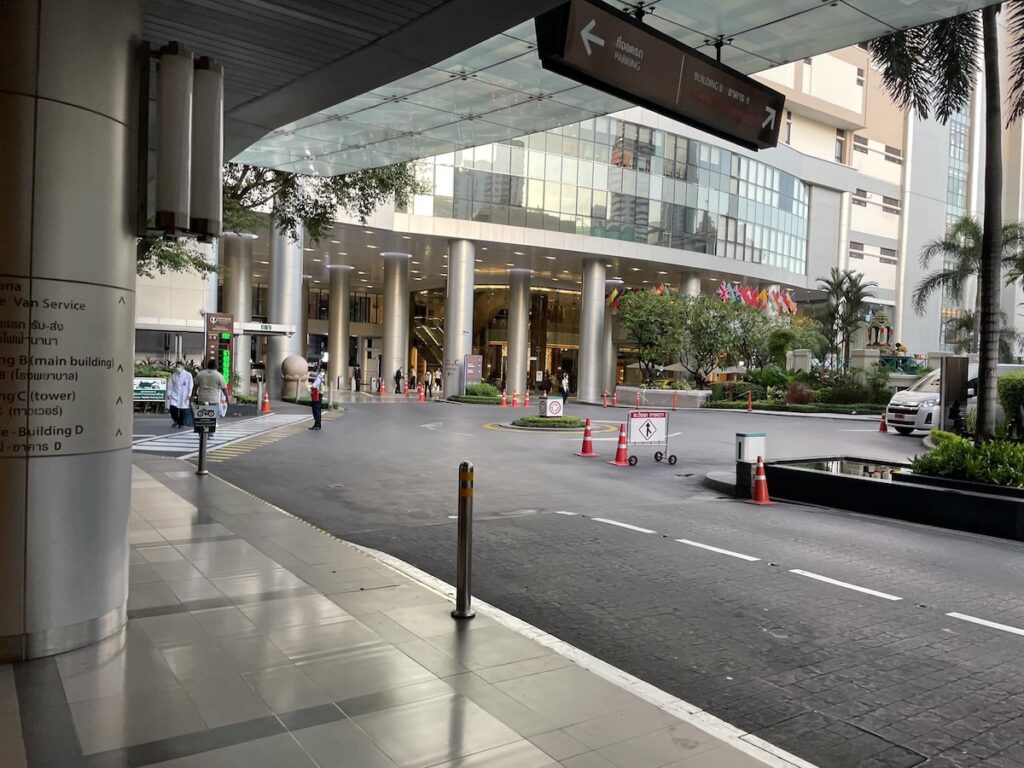 Entrée principale et voies d'accès du Bumrungrad International Hospital, un grand complexe hospitalier moderne à Bangkok avec des drapeaux internationaux.