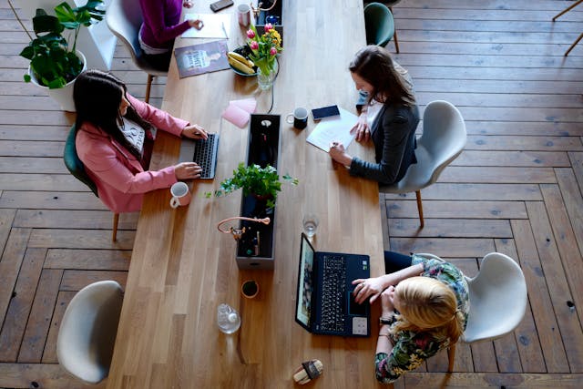 Des digital nomads travaillant ensemble sur leurs ordinateurs portables autour d'une grande table dans un espace de coworking lumineux et moderne.