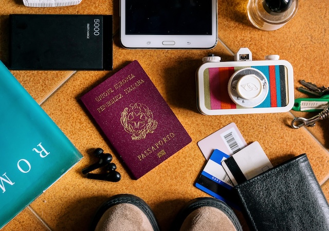 Vue de dessus des essentiels de voyage pour l'Asie : passeport, smartphone, portefeuille, appareil photo et guide de voyage posés au sol.