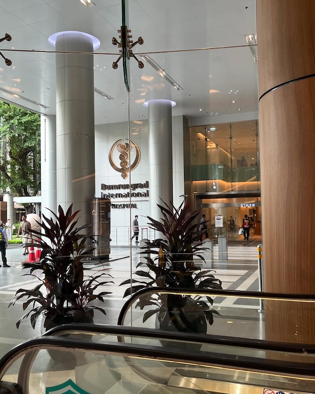Vue de l'entrée principale de l'hôpital international Bumrungrad à Bangkok, montrant des colonnes modernes et le logo, illustrant les standards élevés et les coûts des soins en Thaïlande.