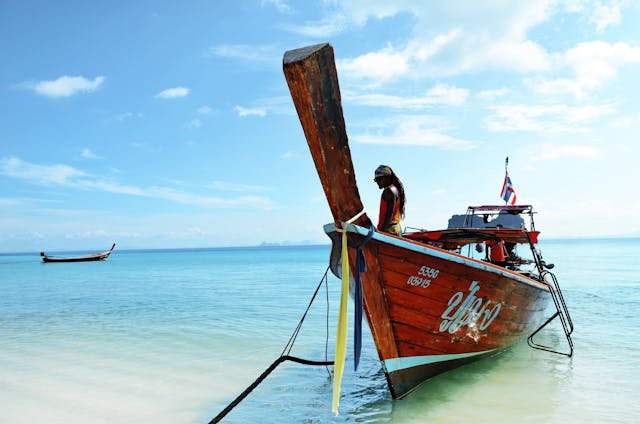Bateau long-tail traditionnel en bois sur une mer turquoise, amarré sur une plage de sable blanc d'une île hors des sentiers battus en Thaïlande.