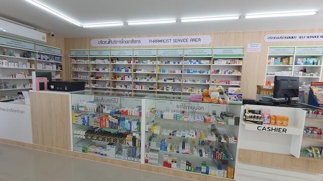 Vue de l'intérieur d'une pharmacie thaïlandaise moderne, montrant des étagères de médicaments bien organisées, un comptoir et des indications claires pour les patients.