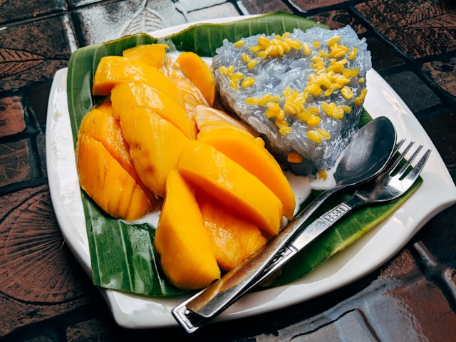 Assiette de Khao Niao Mamuang avec de la mangue fraîche découpée, du riz gluant bleu et une sauce au lait de coco.