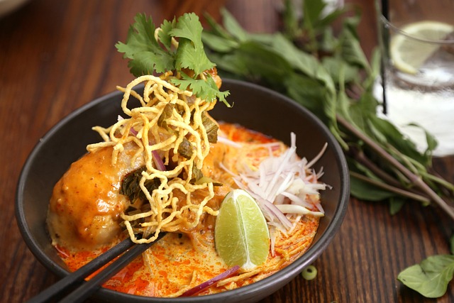 Bol de Khao Soi avec pilon de poulet, nouilles croustillantes et un quartier de citron vert, plat typique de Chiang Mai.