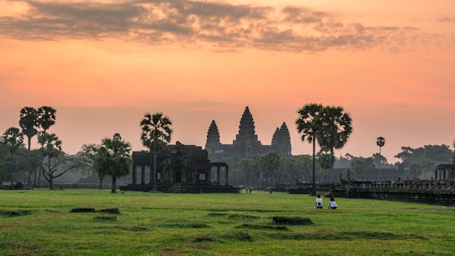 Vue panoramique des temples d'Angkor Wat au Cambodge au lever du soleil, avec des palmiers et une vaste pelouse au premier plan.