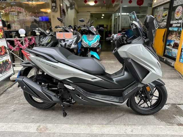 Scooter Honda Forza gris garé devant une boutique de location en Thaïlande, illustrant les risques liés à la conduite de deux-roues et la nécessité d'une bonne couverture d'assurance.