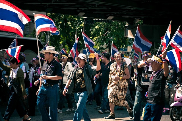 Rassemblement de personnes brandissant des drapeaux thaïlandais dans une rue urbaine lors d'une manifestation.