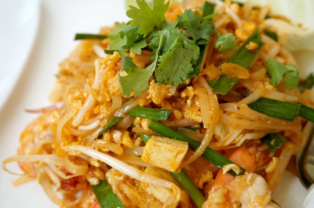 Gros plan sur une assiette de Pad Thai avec des crevettes, du tofu frit, des pousses de soja et de la ciboulette.