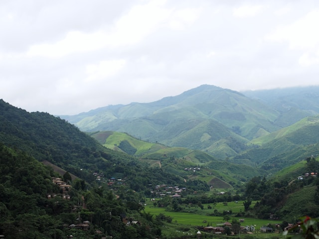 Paysage de montagnes verdoyantes avec un village et des rizières dans une vallée, illustration d'une destination hors des sentiers battus dans la province de Nan en Thaïlande.