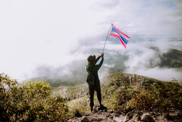 Un randonneur au sommet d'une montagne en Thaïlande, brandissant le drapeau national au-dessus d'une mer de nuages.