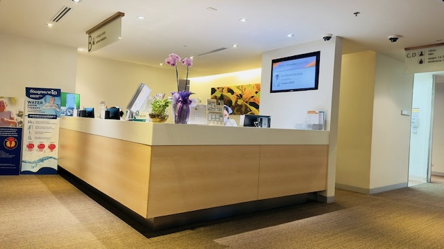 Comptoir d'accueil moderne et lumineux au Bumrungrad International Hospital à Bangkok, avec une infirmière prête à assister les patients.