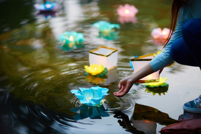 Une personne dépose délicatement un krathong illuminé sur l'eau pour participer au rituel du festival Loi Krathong.