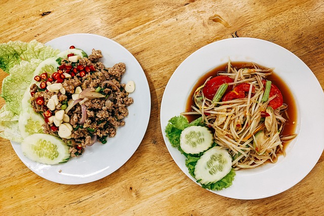 Deux assiettes de plats d'Isaan sur une table en bois : une salade de papaye Som Tam et une salade de viande hachée Laab.