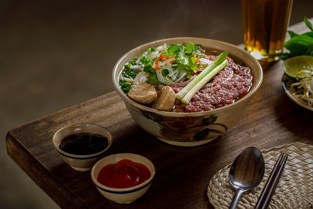 Un bol fumant de soupe Phở vietnamienne avec du bœuf, des boulettes, des nouilles de riz et des herbes fraîches, servi avec des sauces pour accompagner.
