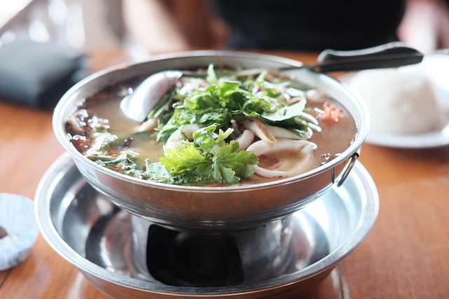 Un bol de soupe thaïlandaise Tom Yum servi chaud dans un réchaud en métal, généreusement garni de coriandre fraîche et d'autres herbes médicinales.